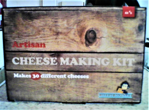 A side view of lidded crate made of wooden planks on which is stamped Artisan (in red lettering) CHEESE MAKING KIT (in upper case white lettering) and Makes 30 different cheeses  (in lower case white lettering).